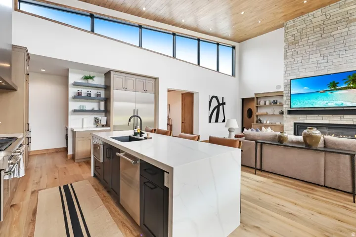 Vaulted wood-paneled ceiling, high-level transom windows, stone-clad fireplace, kitchen island with integrated sink, and wood-finish flooring