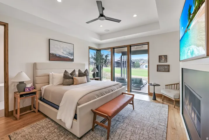Recessed lighting with a ceiling fan, tray ceiling, wood-finish flooring, built-in fireplace, and expansive glass doors