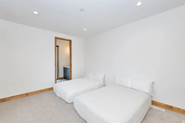 Recessed lighting, wood trim, wall-to-wall carpeting, and an adjacent bathroom with patterned floor tile and a vanity