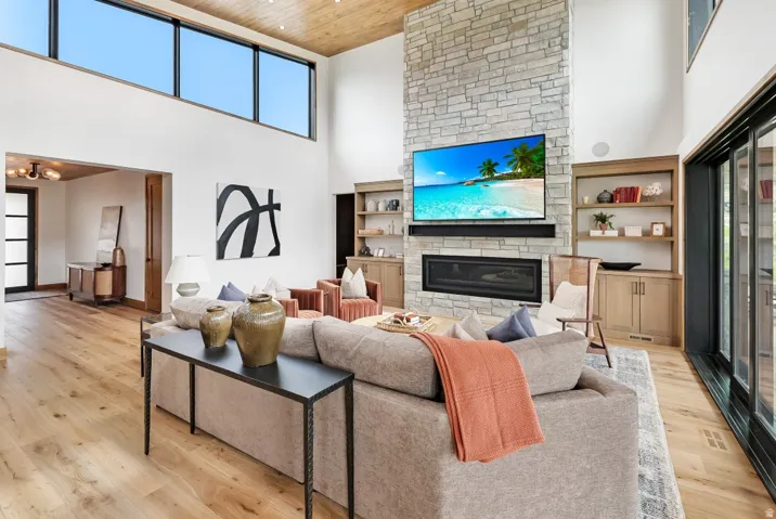Open-concept living space anchored by a wood-burning fireplace with stacked stone surround and a wall-mounted flat-screen television
