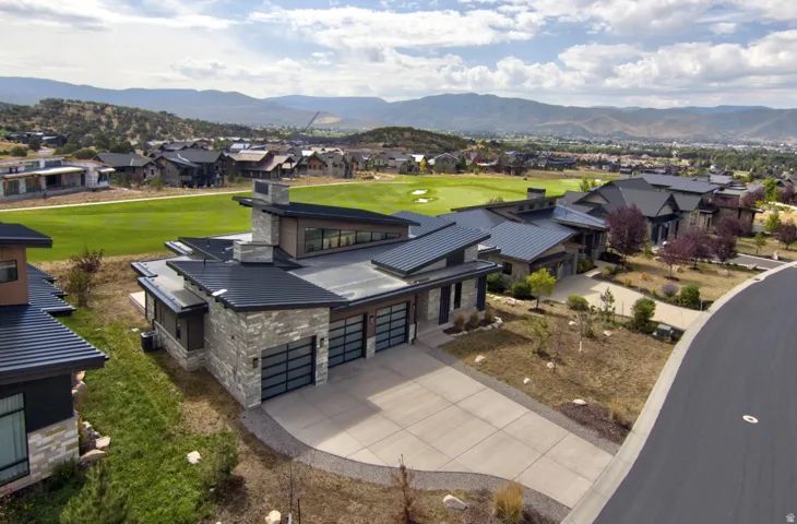 Modern architecture featuring multiple rooflines, stone and wood-look exterior finishes, a multi-car garage, and a concrete driveway