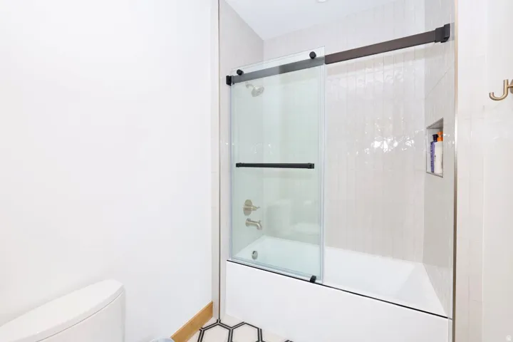 Modern bathroom featuring a frameless glass sliding shower enclosure with brushed metal hardware, white subway tile surround, and a sleek vanity setup with integrated storage and brushed brass fixtures