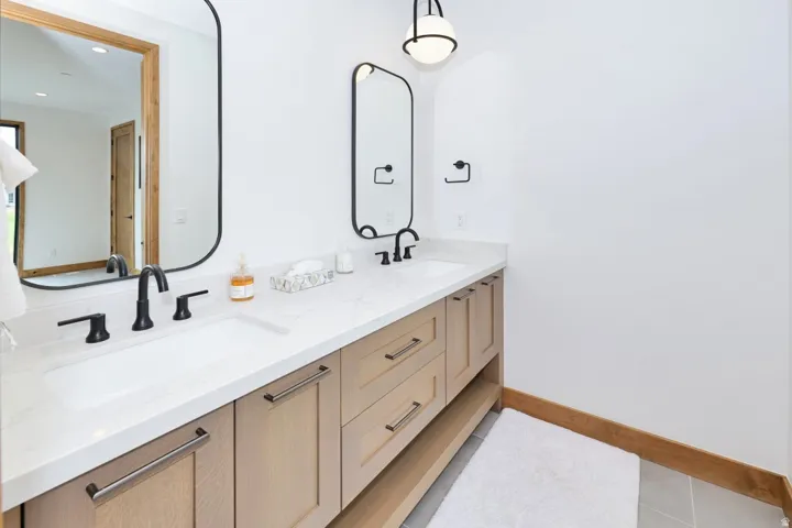 Dual vanity with light wood-finish cabinetry, integrated sinks, black fixtures, and white countertops
