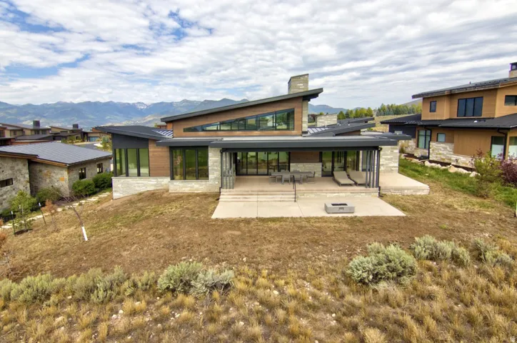 Modern architectural design featuring expansive glass panels, a covered patio, and a stone-clad exterior
