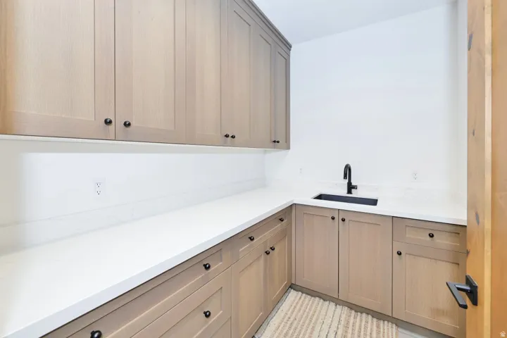 Extensive white countertops, light wood-finish cabinetry, black basin sink, matte black faucet, and matte black cabinet hardware