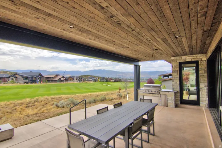 Covered patio featuring a wood-paneled ceiling with recessed lighting, an outdoor kitchen with a built-in grill, and a stone accent wall