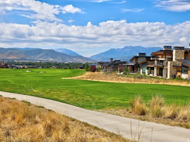 Expansive green lawn with mature landscaping and natural dry grasses, situated against a backdrop of distant mountain ranges