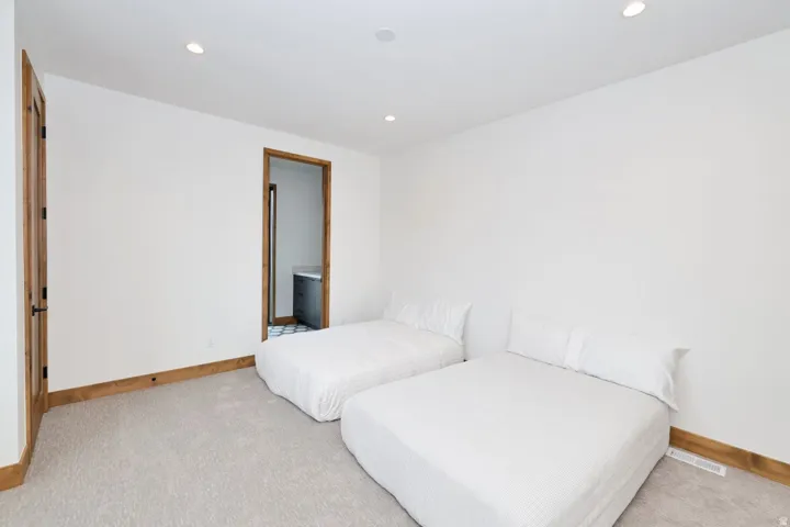 Bright secondary bedroom featuring dual twin beds with crisp white bedding, neutral carpet flooring, and warm wood-trim framing