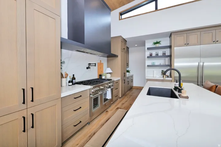 Gourmet kitchen featuring a large island with an undermount sink, stainless steel appliances, wood-finish flooring, and a vaulted ceiling with an upper window