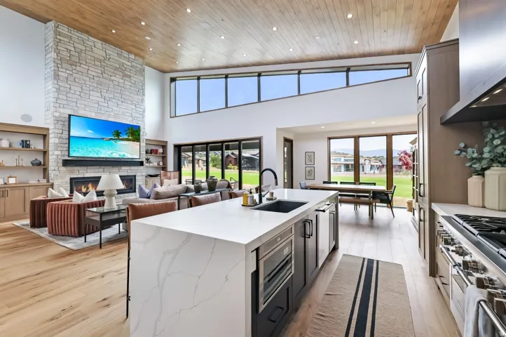 Open-concept interior featuring wood-finish flooring, a vaulted wood-paneled ceiling, and a stone-clad fireplace