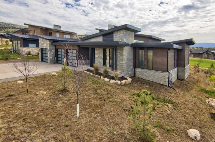 Contemporary exterior with stone veneer and wood-finish siding, featuring a multi-level roofline, attached garage with glass panel doors, and a concrete driveway
