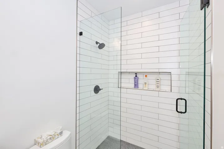 Spa-inspired shower featuring subway tile walls, frameless glass enclosure, built-in recessed niche with shelving, dual showerheads with modern matte black fixtures, and non-slip floor surface