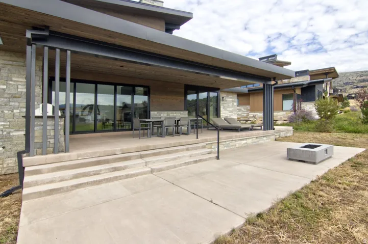 Expansive patio with multi-level concrete steps, a built-in outdoor grill, and a rectangular fire pit
