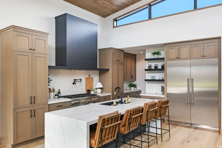 Spacious kitchen featuring a large waterfall island with seating, stainless steel appliances, a black range hood, and wood-finish flooring