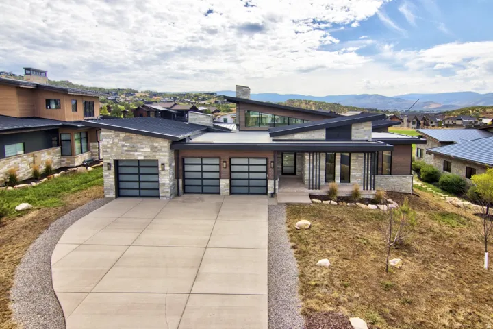 Modern exterior with stone and wood-finish siding, multi-pane garage doors, a concrete driveway, and a low-sloped roofline