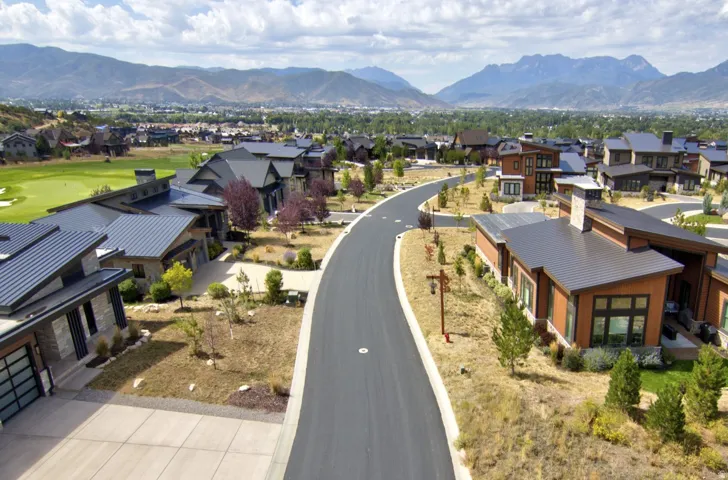 Contemporary residential architecture, metal roofs, paved roadway, mountain backdrop, and green landscaping