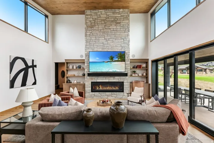 Vaulted wood-paneled ceiling, floor-to-ceiling stone fireplace with gas insert, built-in shelving, and expansive sliding glass doors