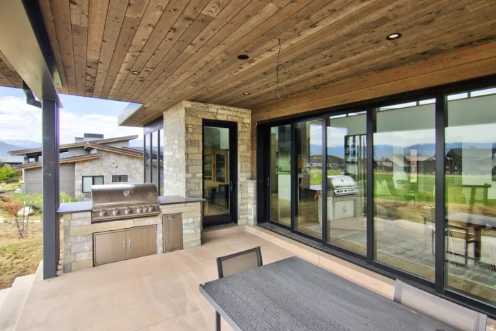 Outdoor patio with a wood-finish ceiling, stone-clad outdoor kitchen, built-in stainless steel grill, and expansive sliding glass doors
