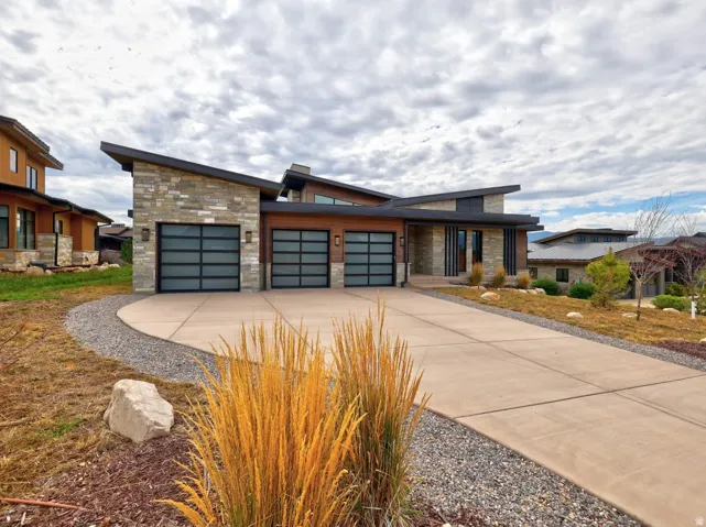 Modern architectural design featuring a stone and wood-finish exterior, a multi-car garage with frosted-panel doors, a concrete driveway, and a sloped roofline