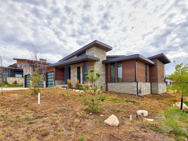 Contemporary architecture featuring wood-paneled siding, stone veneer accents, an attached garage with glass panel doors, and a covered entry