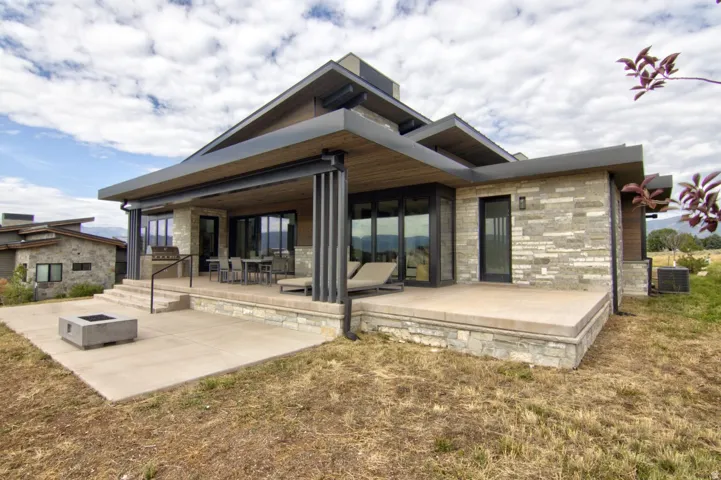 Stone veneer exterior with a covered patio, multiple glass sliding doors, and a concrete paver patio