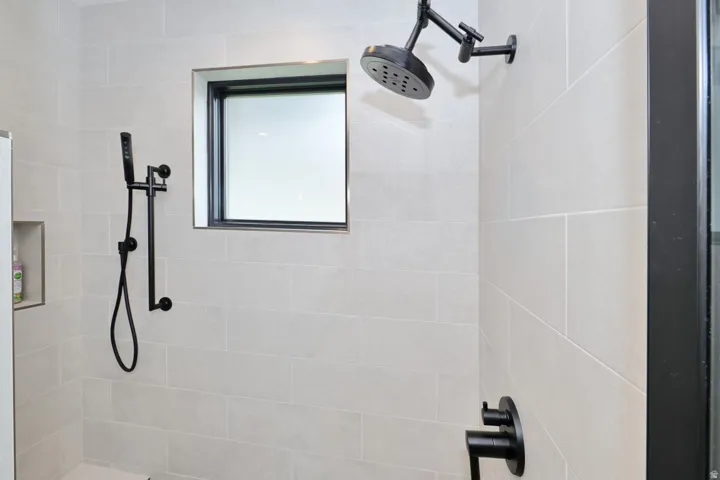 Tiled shower with matte black fixtures, including a rainfall showerhead and handheld shower