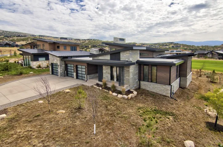 Contemporary architectural style featuring a multi-level design, stone and wood-finish siding, multiple flat roofs, and a concrete driveway
