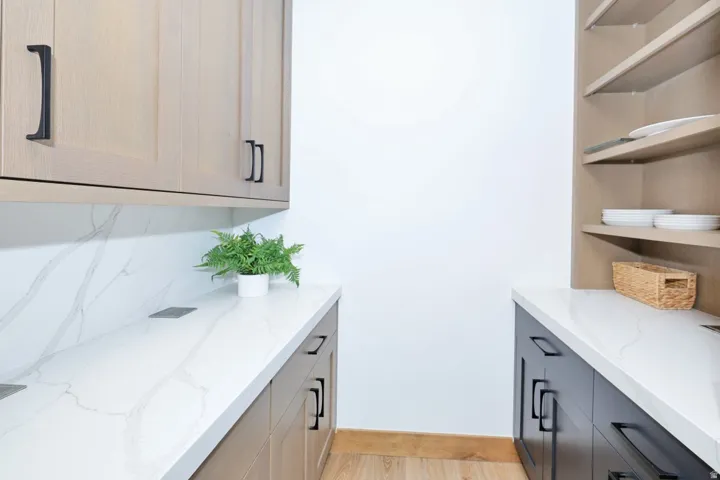 White countertops with subtle veining, light wood-finish upper cabinetry, black lower cabinetry, white wall, and open shelving