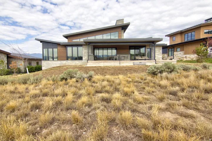 Modern architectural design featuring expansive windows, natural wood-finish siding, stone accents, and a large covered outdoor patio