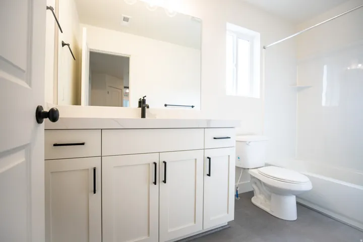 Full secondary bath with painted white wood cabinets and quartz slab countertops.