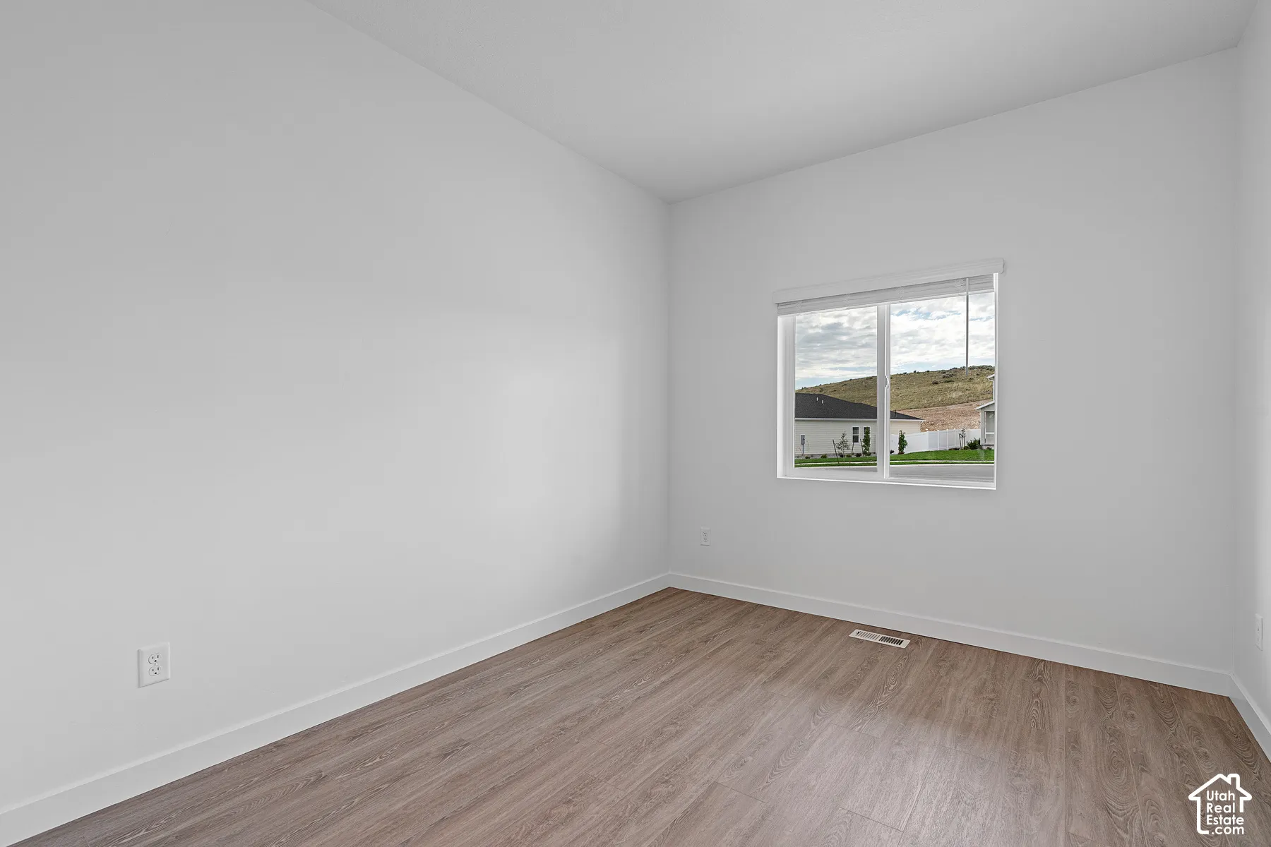 Light-filled room featuring wood-finish flooring, white walls, and a large window with white blinds