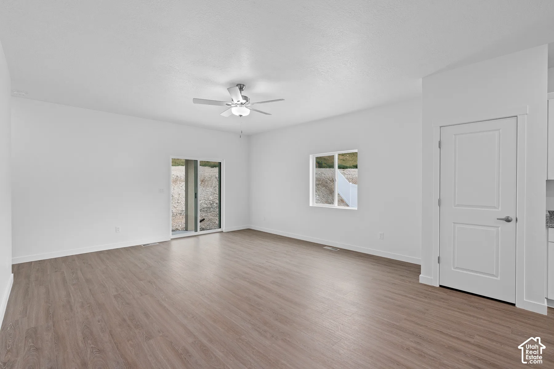 Spacious room featuring wood-finish flooring, a contemporary ceiling fan, and a sliding glass door