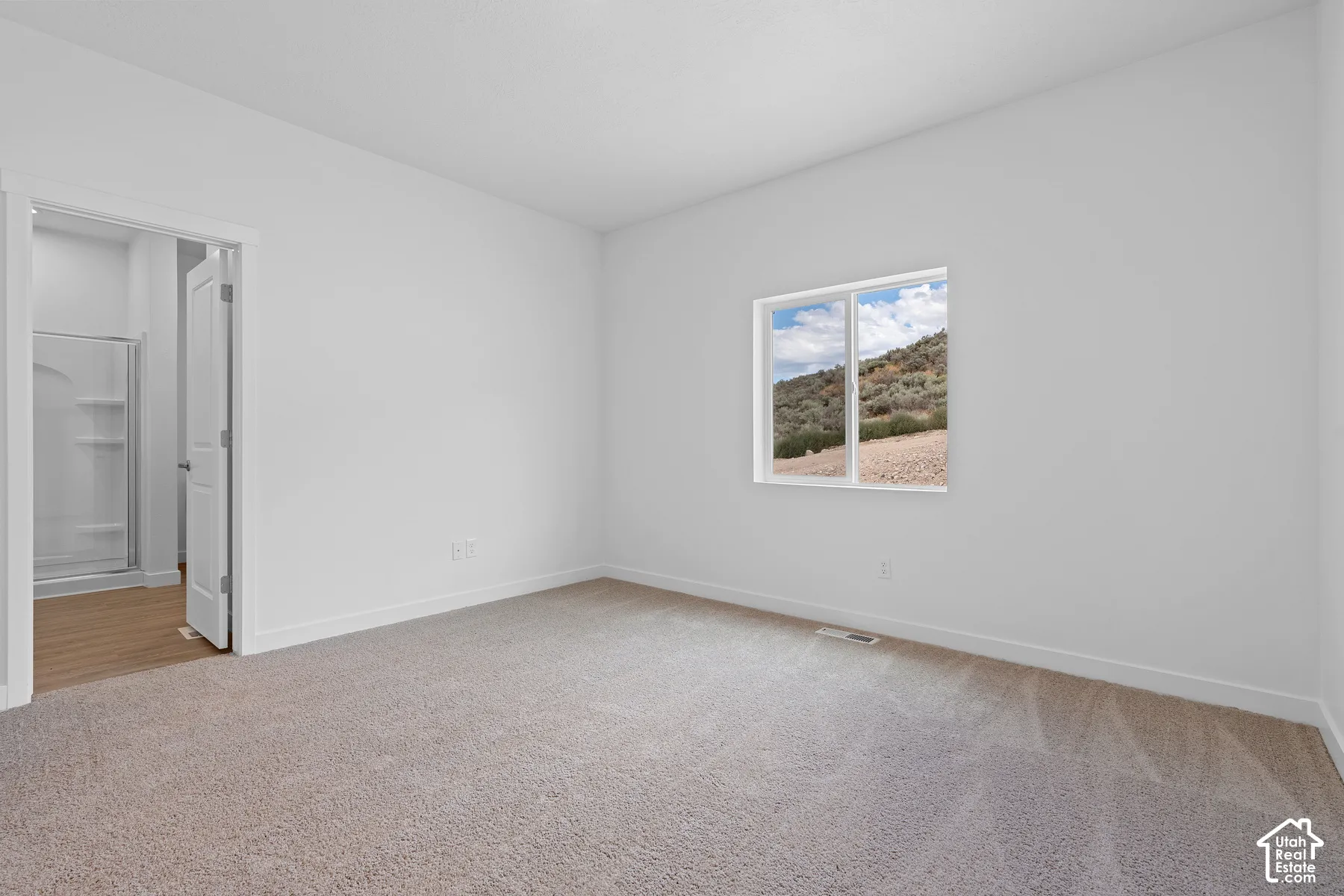 Neutral wall colors, carpeted flooring, window with natural scenery, and an en-suite bathroom with a shower enclosure and wood-finish flooring