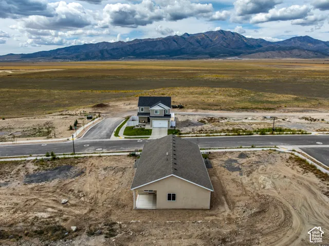 Mountain backdrop, newly constructed residence with attached garage, paved street, and undeveloped property
