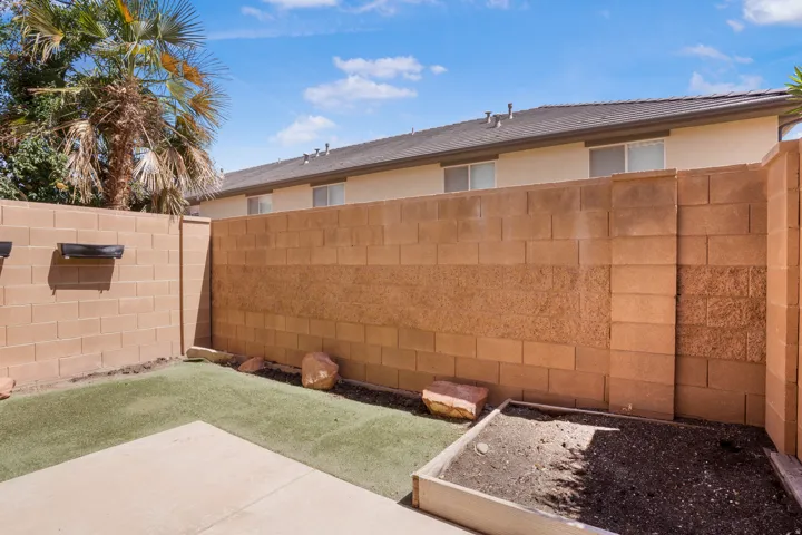 Enclosed patio featuring concrete block walls, a concrete slab, artificial turf, and a raised planter box