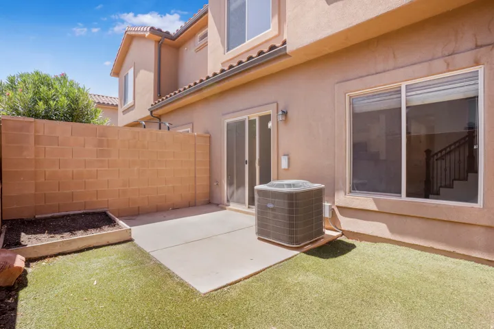 Private backyard featuring artificial turf, a concrete patio, a block wall, and an integrated planter box