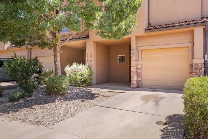 Stucco exterior with stone accents, concrete driveway, attached garage, and mature landscaping with rock ground cover