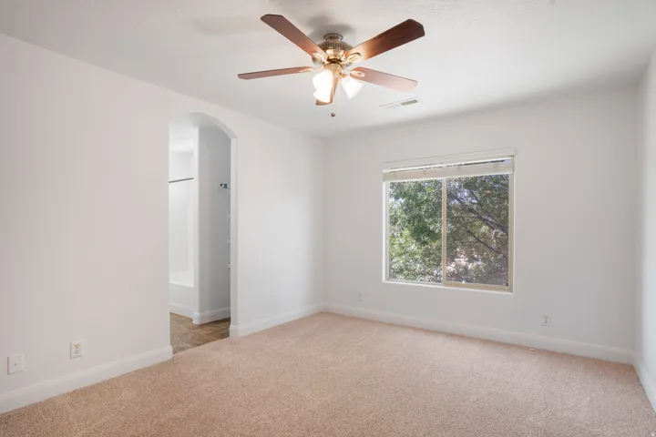 Carpeted flooring, arched doorway, ceiling fan, and window