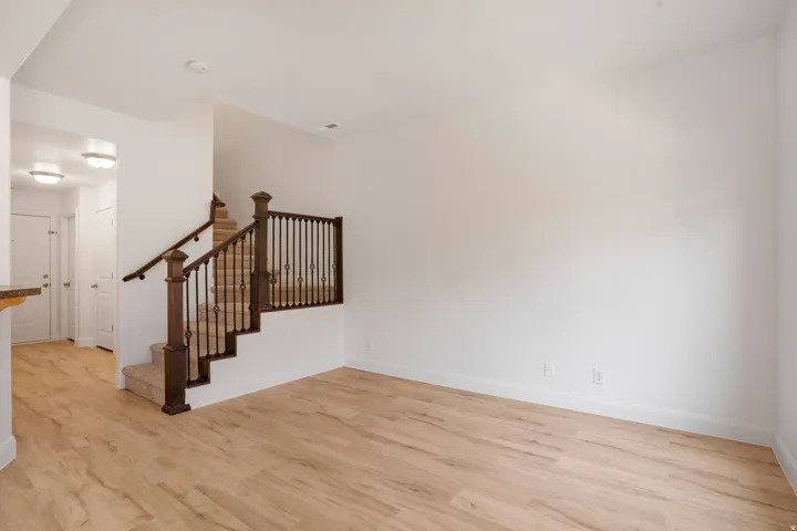 Light wood-finish flooring, white walls, carpeted staircase with wood newel posts, and wrought iron balusters