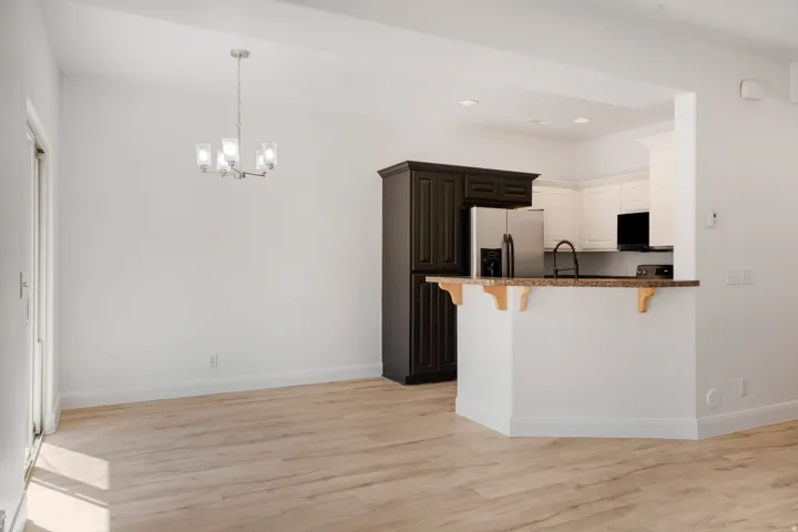 Bright interiors with light wood-finish flooring, a kitchen featuring white upper cabinetry, dark lower cabinetry, and stainless steel appliances