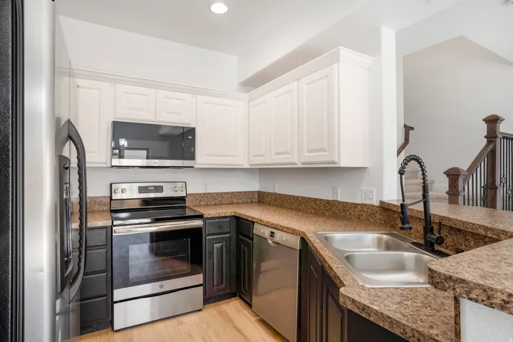 Kitchen featuring stainless steel appliances, dual-tone cabinetry, composite countertops, and a double-basin sink with a matte black pull-down faucet