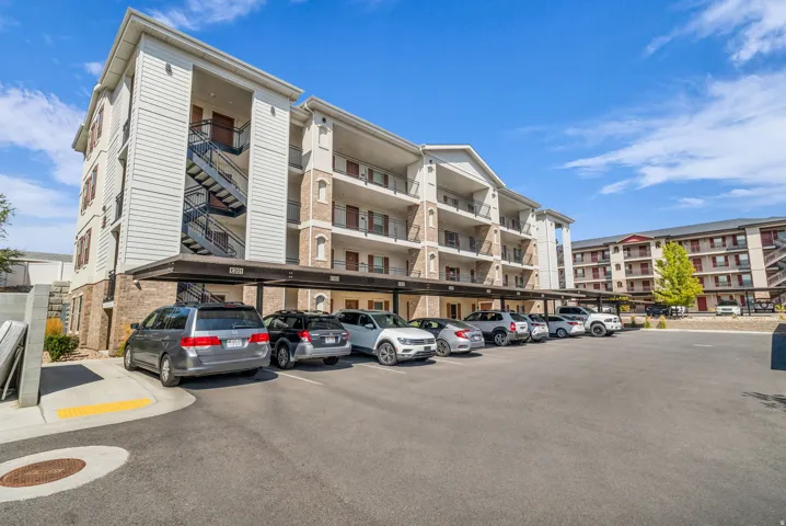 Modern multi-story residential complex featuring clean architectural lines, horizontal balconies with metal railings, and light-colored exterior cladding