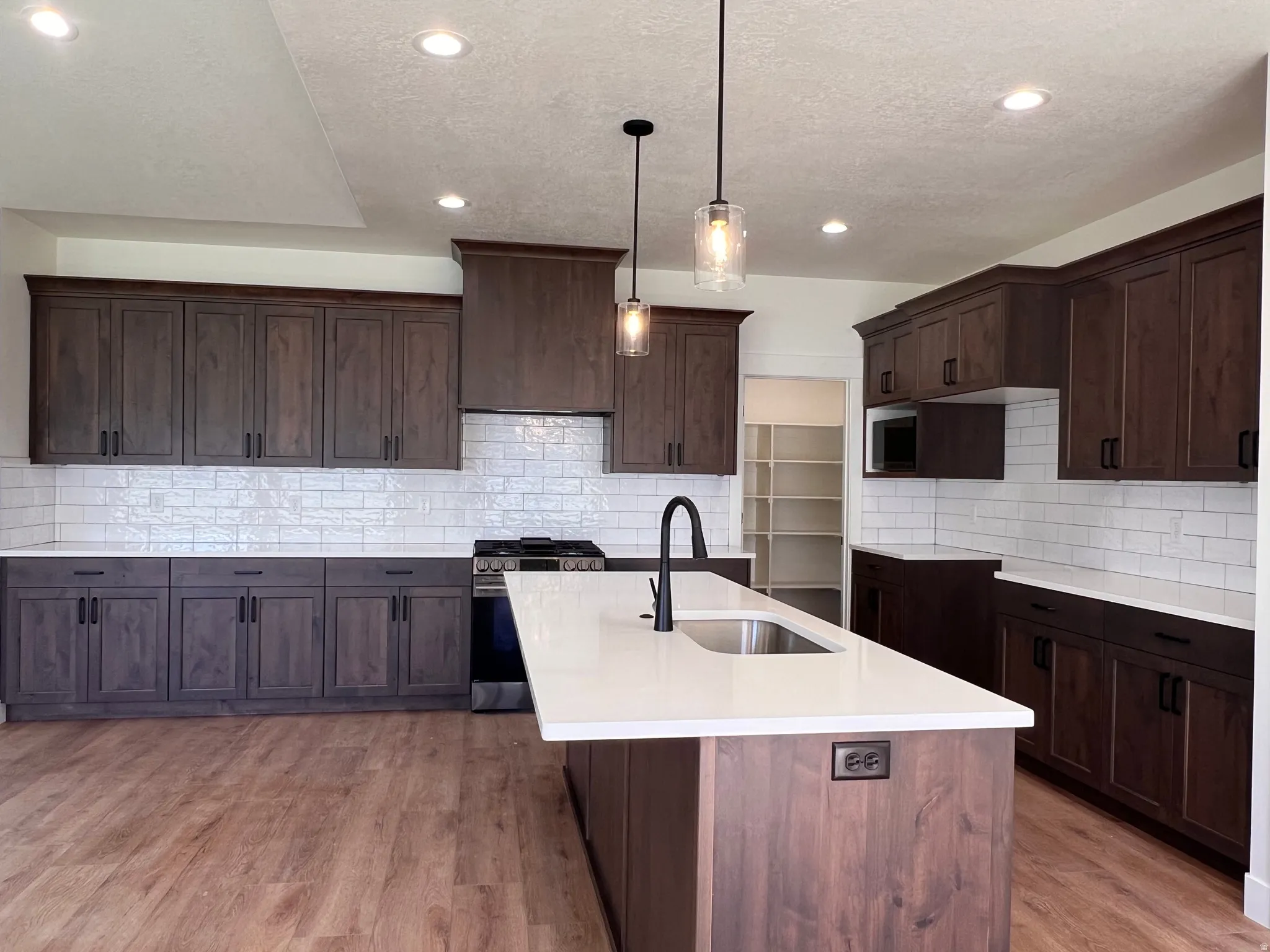 Kitchen featuring dark wood-finish cabinetry, white countertops, a subway tile backsplash, and wood-finish flooring