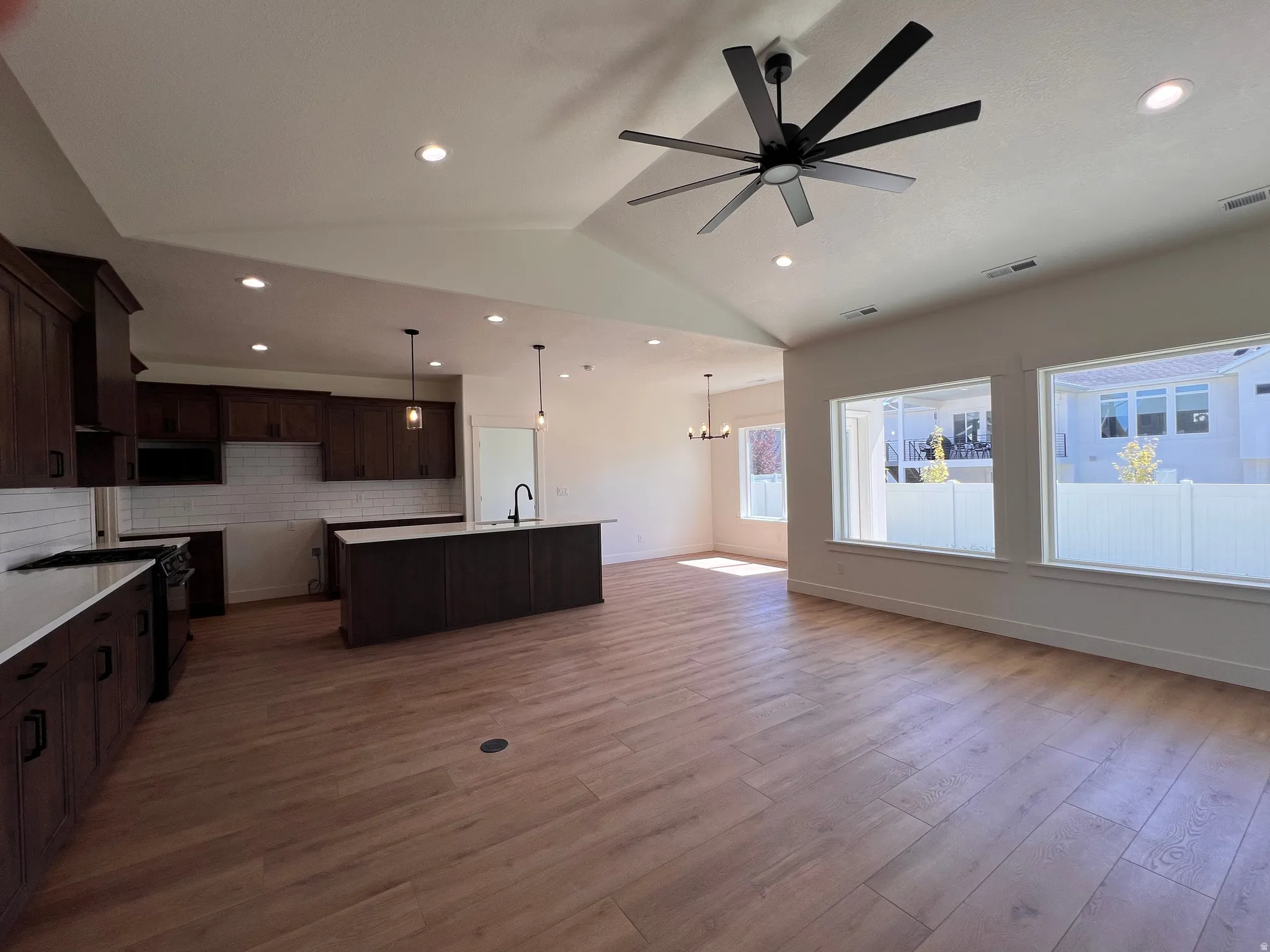 Vaulted ceiling with a contemporary ceiling fan, recessed lighting, wood-finish flooring, dark wood cabinetry, and a kitchen island with pendant lighting