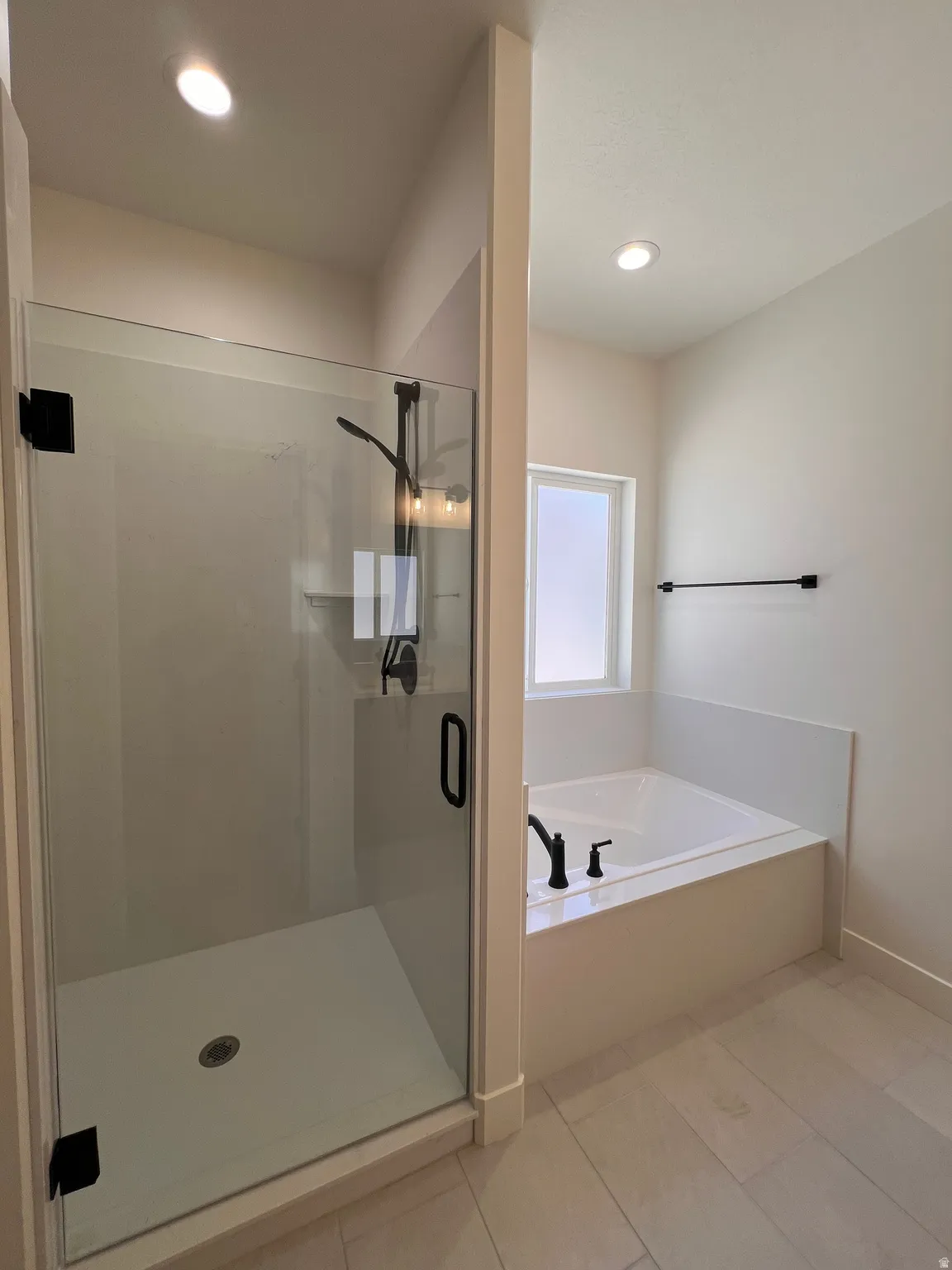 Walk-in shower with clear glass enclosure and matte black hardware, built-in soaking tub with matte black fixtures, and light-toned tile flooring