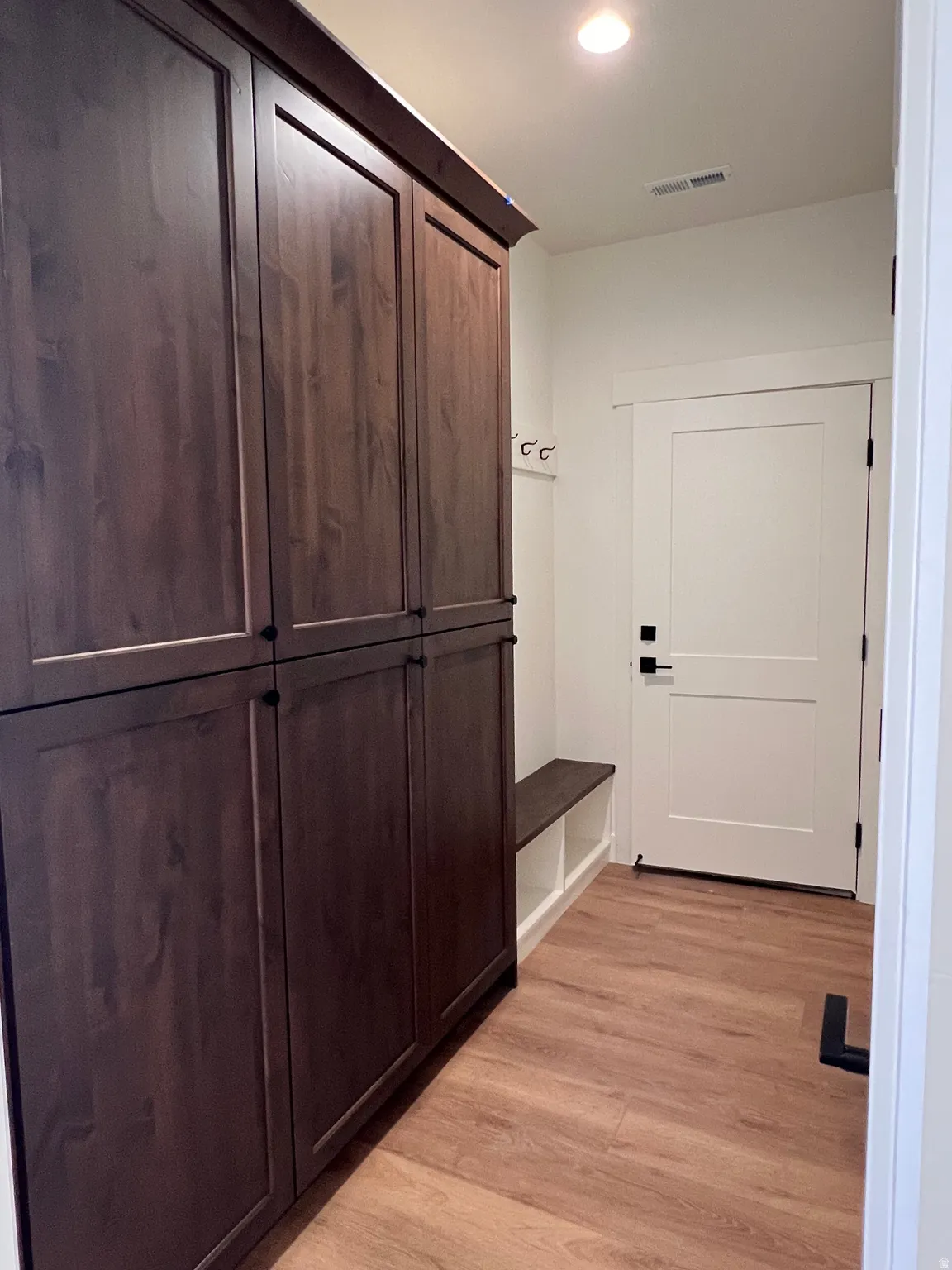 Wood-finish flooring, built-in storage cabinetry, recessed lighting, and a solid core door with matte black hardware