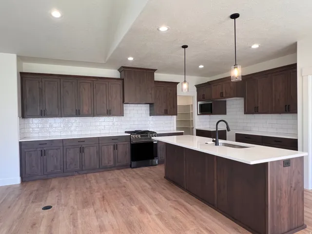 Spacious kitchen featuring wood-finish flooring, ample cabinetry, white subway tile backsplash, and a large island with a sink and pendant lighting