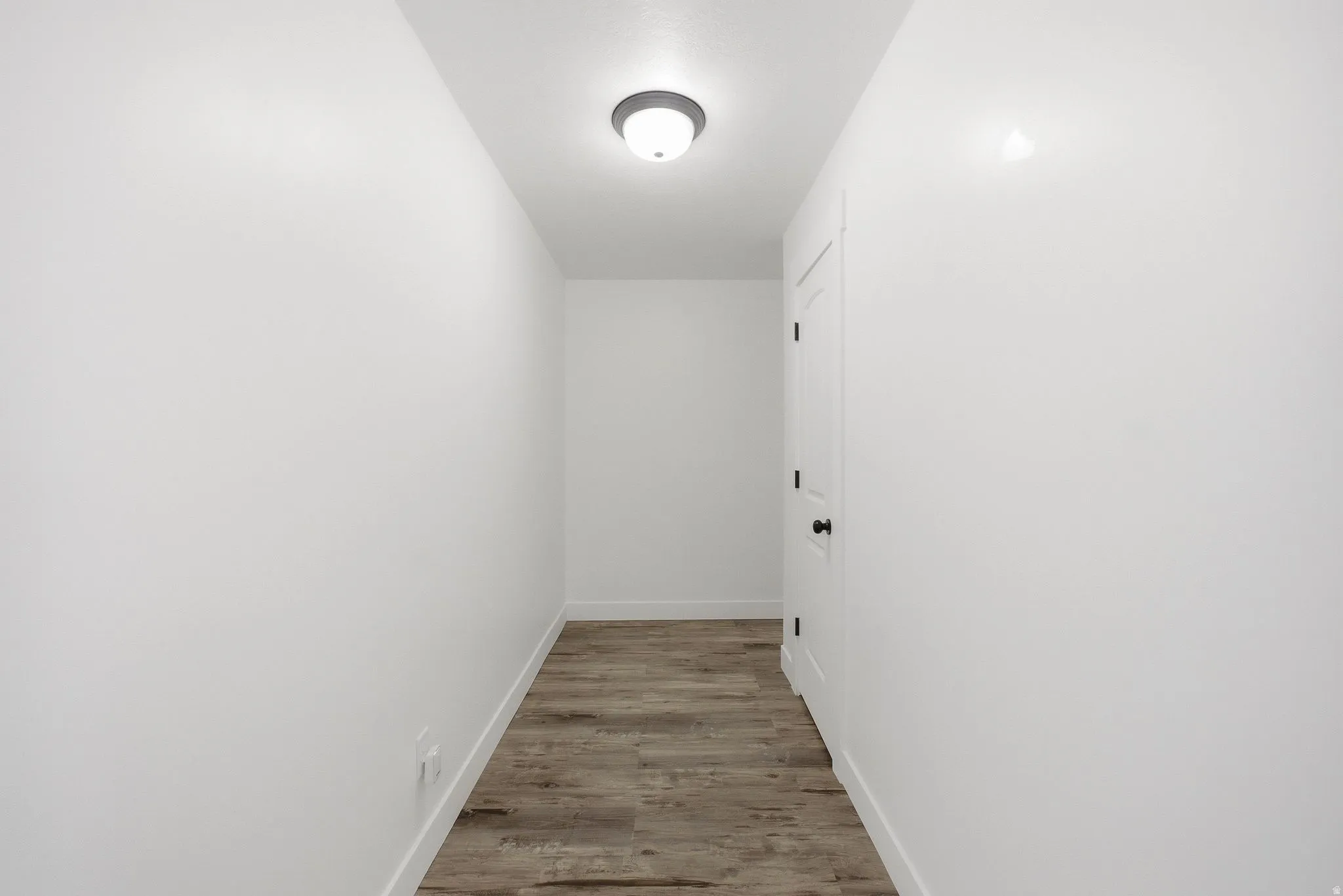 Hallway featuring wood-finish flooring, white walls, and a flush-mount ceiling light
