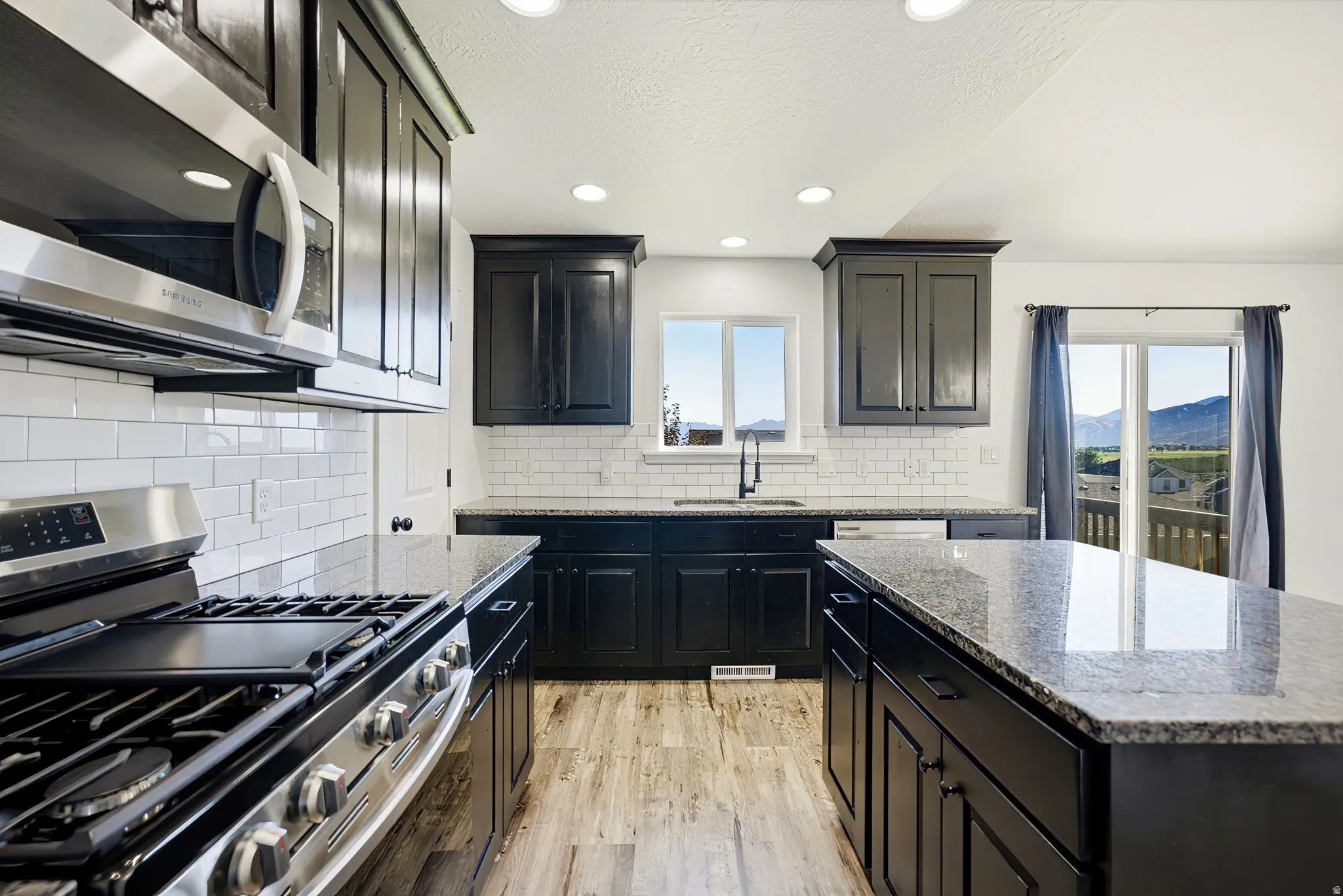 Kitchen featuring dark cabinetry, light-toned wood-finish flooring, stainless steel appliances, a subway tile backsplash, and a center island with a stone countertop