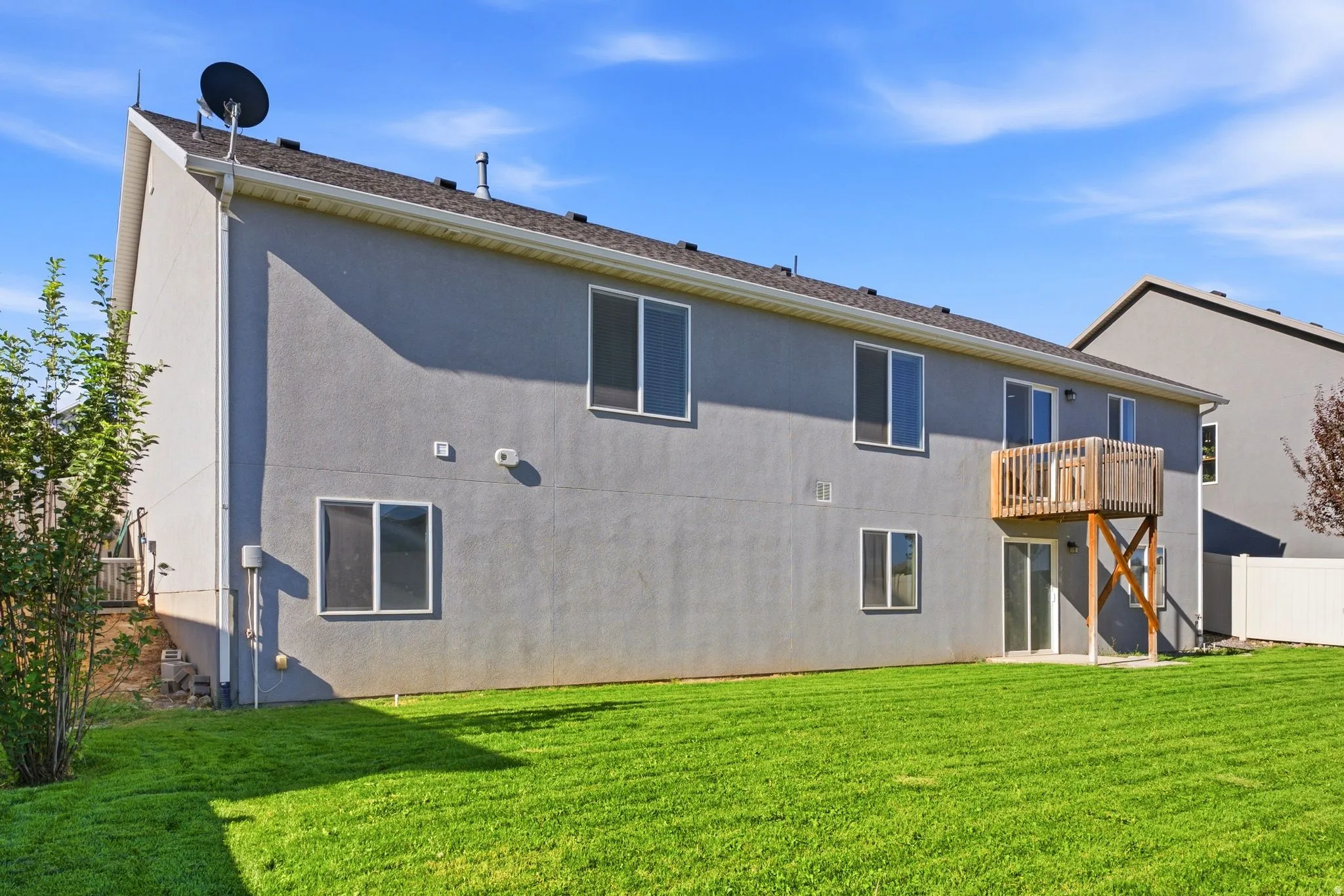Expansive green lawn with a stucco exterior, multiple windows, and an elevated wood deck